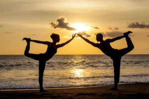 Couple doing exercise yoga together stretching while sunset